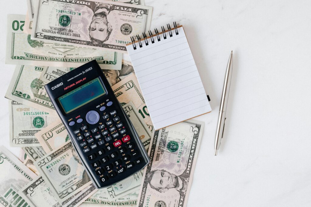 Top view of electronic calculator and notepad placed over United States dollar cash money together with metallic pen for budget planning and calculation